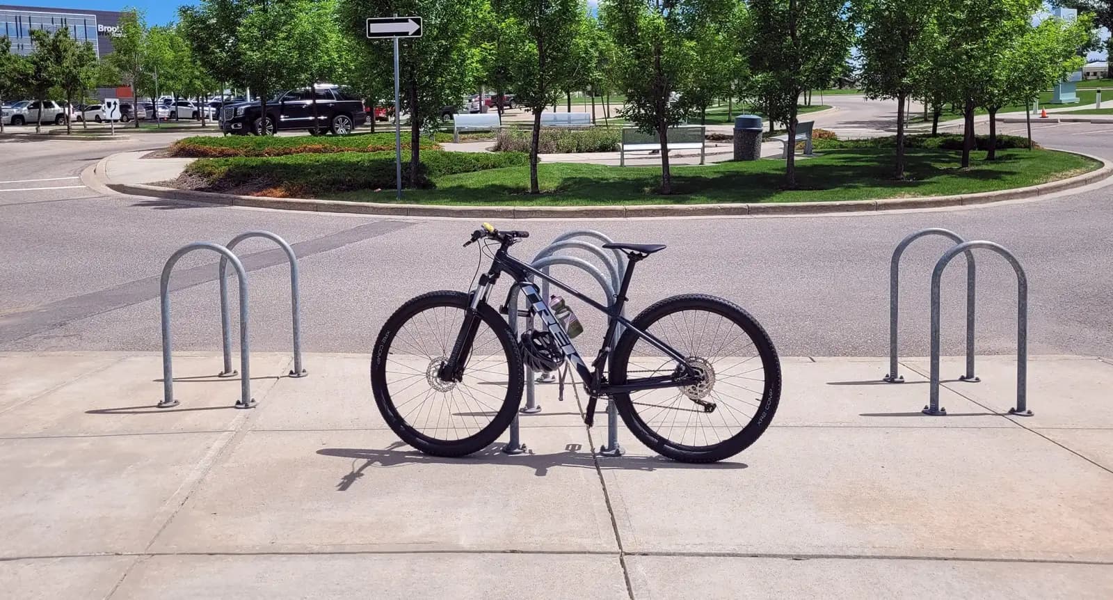 Galvanized steel inverted-U bike racks installed on a sidewalk near a park with green landscaping in Canada